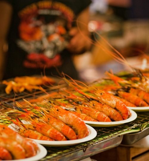 Deliciously grilled shrimps on plates ready to serve at a vibrant Bangkok street food market.