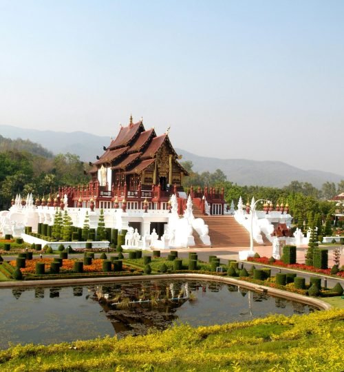 A beautiful Thai temple amidst lush gardens and a reflecting pond in daylight.