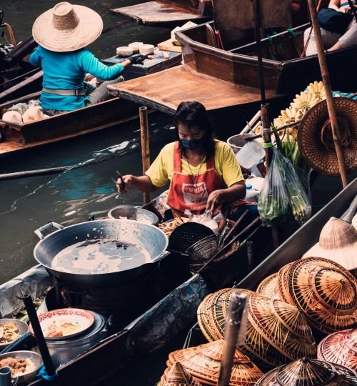 Traditional floating market in Bangkok featuring vendors selling hats and food from boats.