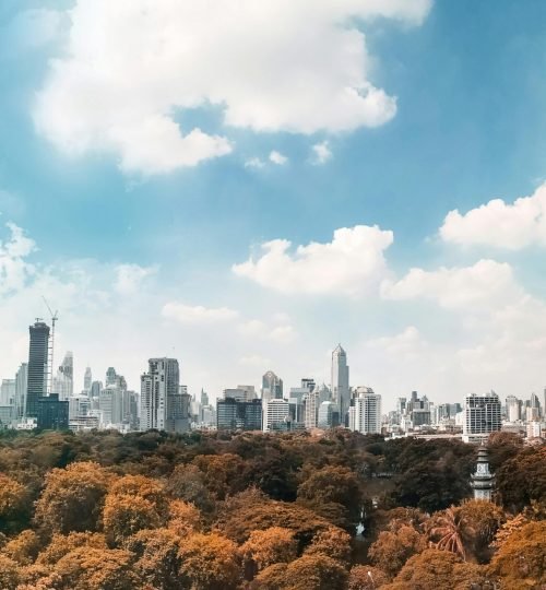 An expansive view of Bangkok's skyline with a vibrant park under a bright blue sky.